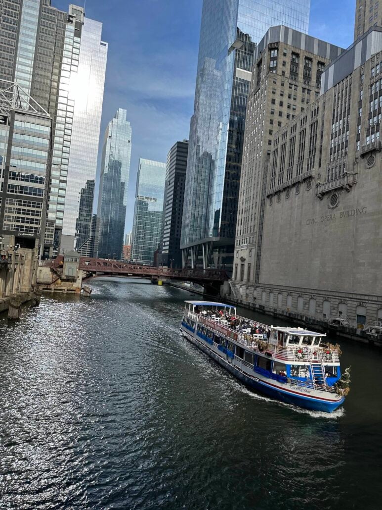 A tour boat travels down the Chicago River past the Civic Opera Building and surrounding skyscrapers.
