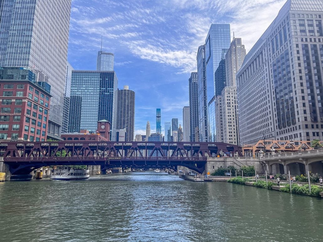 A steel truss bridge crosses the Chicago River, framed by skyscrapers often seen on a Chicago Architecture Boat Tour under a blue sky with light clouds.